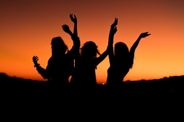 silueta de tres personas en un atardecer levantando los brazos.